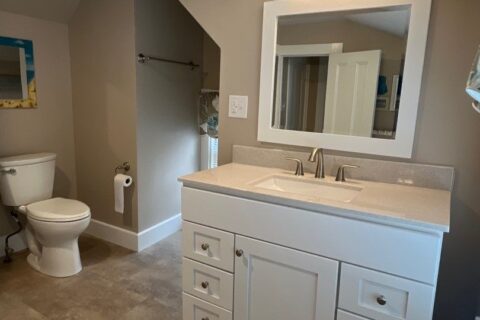 A remodeled bathroom with hardwood floors and a white vanity below a mirror with overhead lighting.