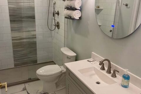 Contemporary bathroom with white vanity, round mirror, glass-enclosed shower, and marble-style tile flooring in MA, RI, and Southern NH