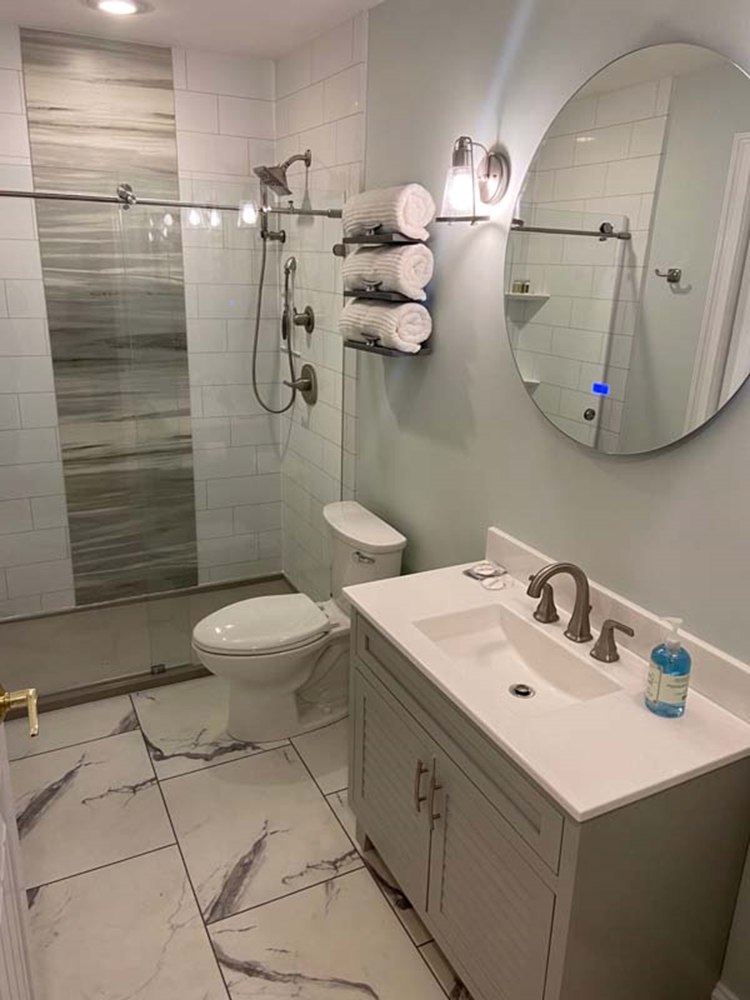 Contemporary bathroom with white vanity, round mirror, glass-enclosed shower, and marble-style tile flooring in MA, RI, and Southern NH