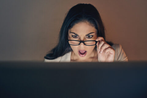 A woman looking surprised over her glasses at a computer.