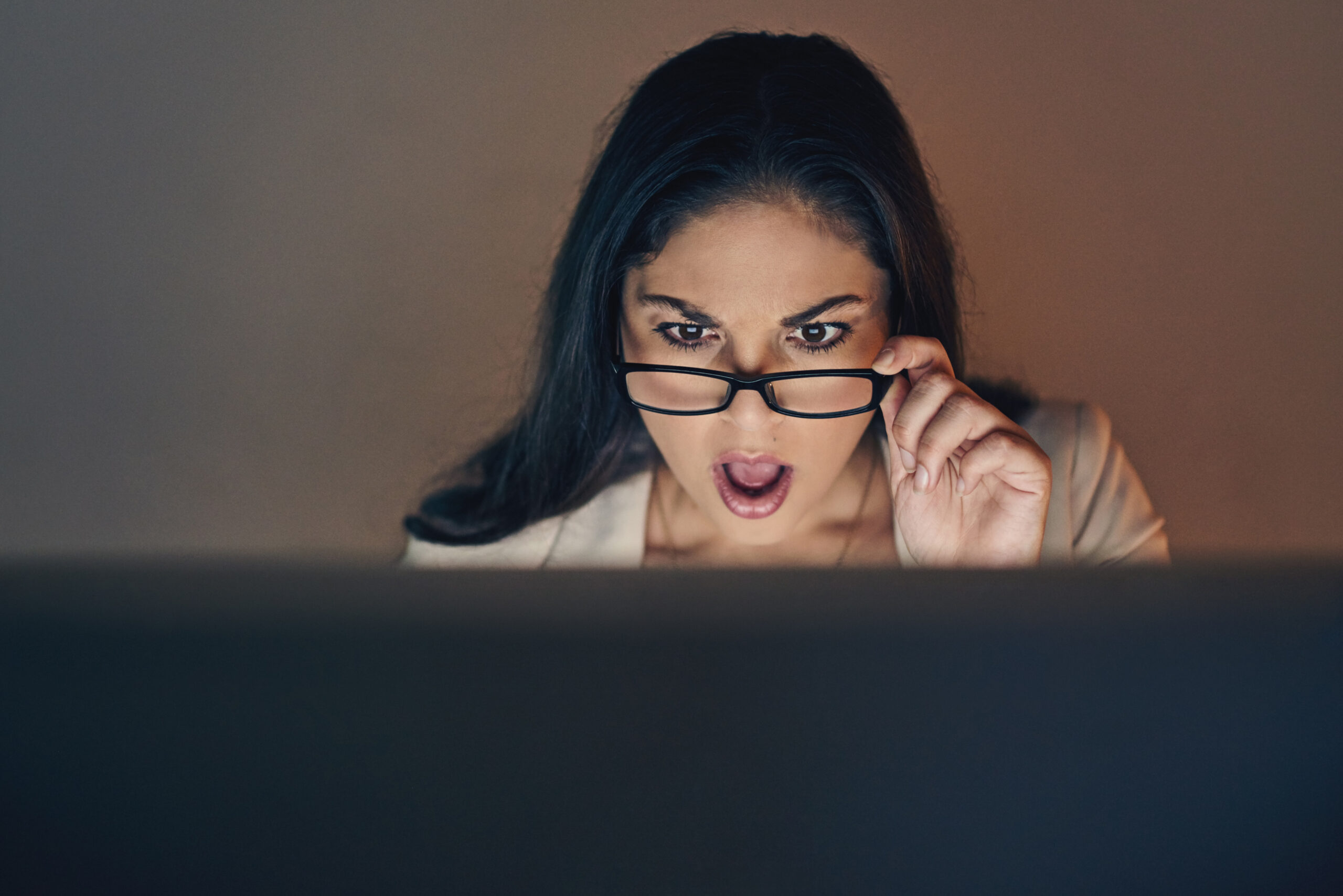 A woman looking surprised over her glasses at a computer.