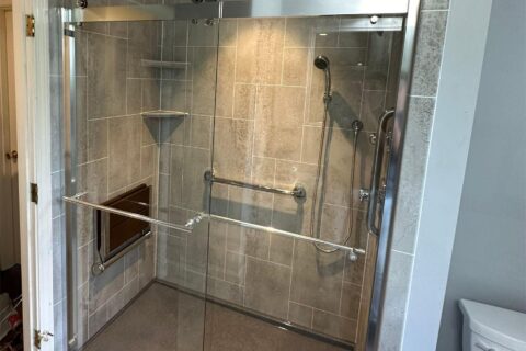 A walk-in shower with a glass door, grab rails, and silver features.