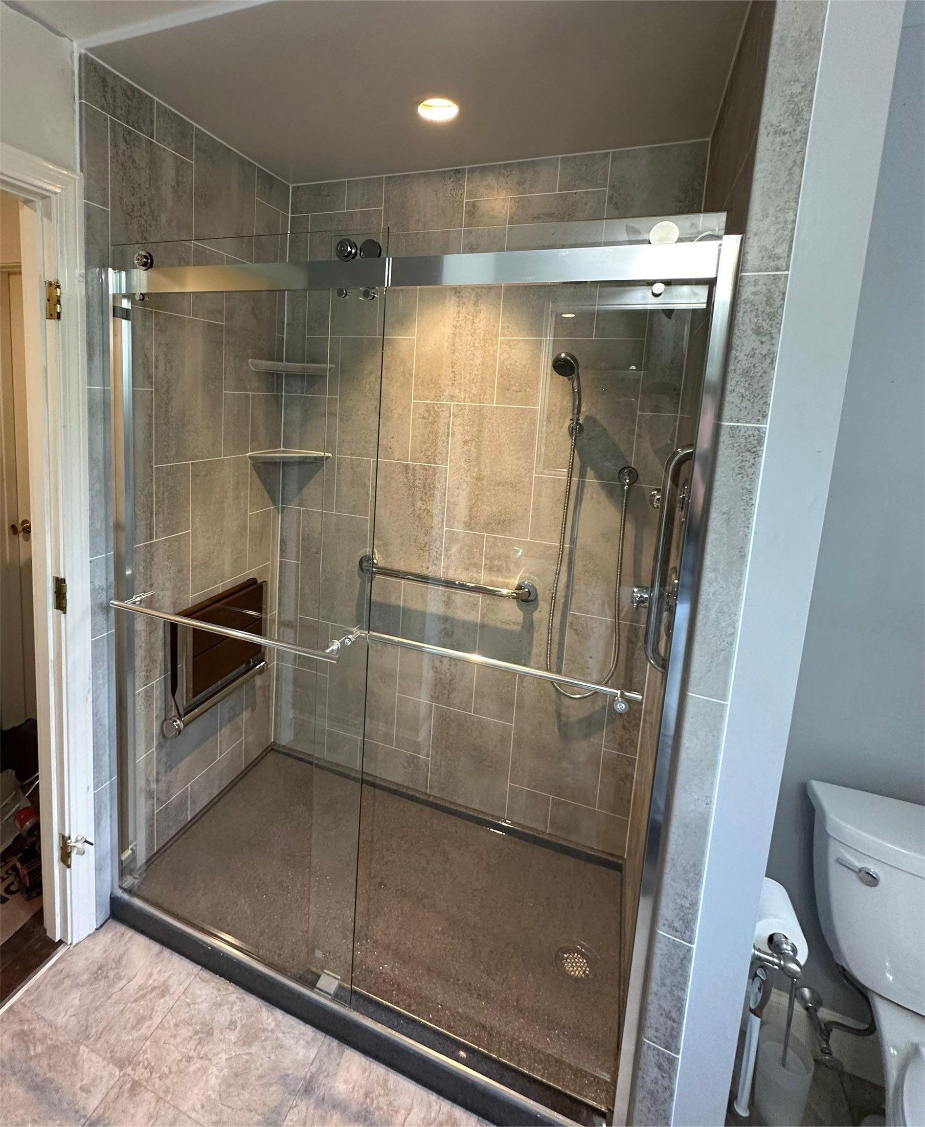 A walk-in shower with a glass door, grab rails, and silver features.